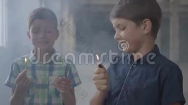 两个可爱的男孩在一个烟雾弥漫的废弃房间里。 一个男孩拿着燃烧的火柴，第二个男孩拿着燃烧的打火机